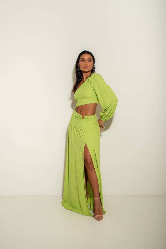 O Vestido Atenas é um modelo de um ombro só, com manga longa, fenda na barriga com detalhe em argola e fenda na perna, oferecendo um visual moderno.