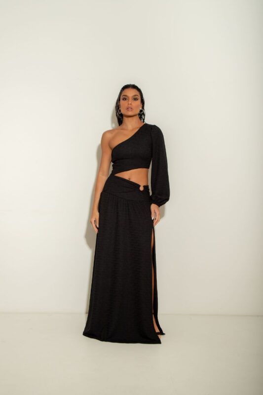 O Vestido Atenas é um modelo de um ombro só, com manga longa, fenda na barriga com detalhe em argola e fenda na perna, oferecendo um visual moderno.